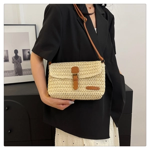 Detail of a straw woven crossbody bag with brown leather flap on a model