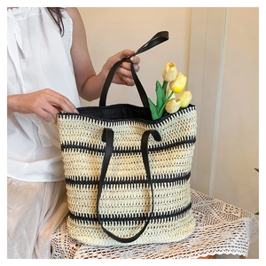 Close-up of a large woven straw tote bag featuring black stripes and thin handles