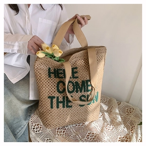Detail of hand-woven straw tote bag featuring green Here Comes The Sun embroidery