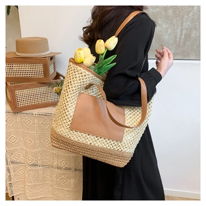 Detail of hollow woven straw tote bag featuring a brown leather pocket and long shoulder strap