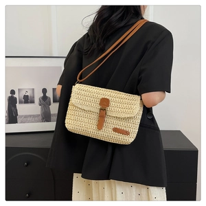 Detail of woven straw crossbody bag with brown leather strap on a model wearing black suit
