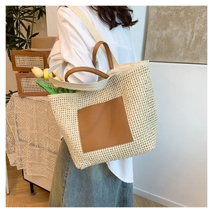 Detail of large straw tote bag with brown leather patch and woven shoulder strap
