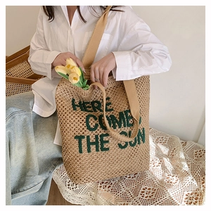 Detail showing the woven straw tote bag with green Here Comes The Sun embroidery