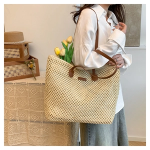 Detailed close-up of handmade woven straw tote bag featuring brown leather straps