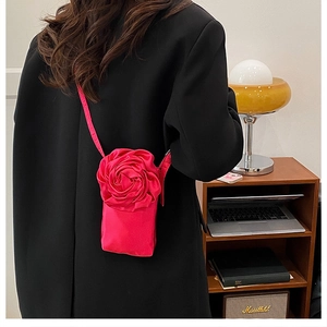 Détail d'un sac bandoulière en satin rose vif avec rose 3D sur un blazer noir