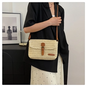 Detailed close-up of woven straw bag with brown leather strap and buckle on a model