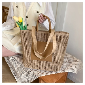 Close-up of woven straw tote bag with brown leather patch and dual handles for summer