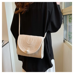 Detail of hand-woven straw crossbody bag with white pearl buckle and cotton strap