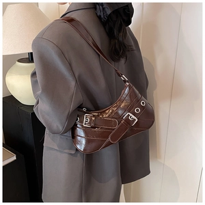 Detail of dark brown patent leather shoulder bag with silver buckles on a female model