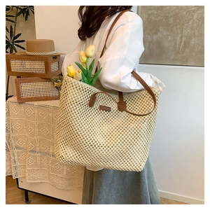 Detail of hand-woven straw tote bag with brown leather handles and minimalist patch