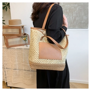 Detail of hollow woven paper straw tote bag with brown leather pocket and dual handles