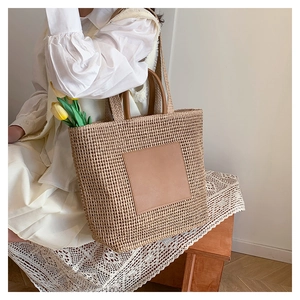 Close-up of Large straw tote bag with brown leather patch and dual woven shoulder straps