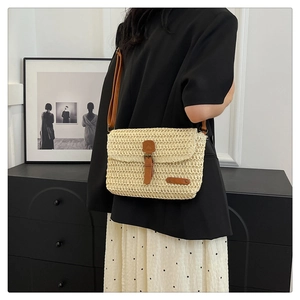 Detail of woven straw crossbody bag with brown leather trim worn by model in black blazer