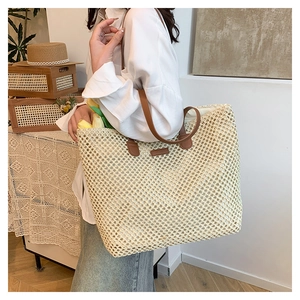 Detail of the woven straw tote bag featuring brown leather straps and mesh texture