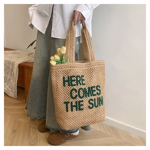 Détail du sac cabas en paille tissé avec texte brodé vert 'HERE COMES THE SUN'