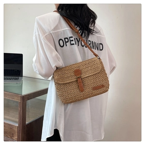 Detail of hand-woven straw crossbody bag with brown leather strap and metal buckle closure