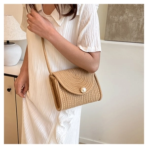 Detail of straw crossbody bag with large pearl accent on white dress model