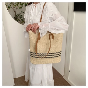 Detail view of woven straw tote bag with black stripes and brown leather handles