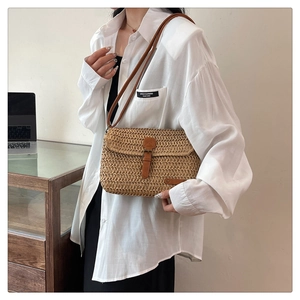 Close-up of woven straw shoulder bag with brown leather strap in a minimalist office setting