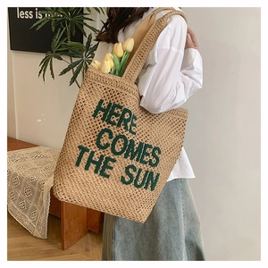 Detail of woven straw tote bag with Here Comes The Sun green embroidery and chic texture