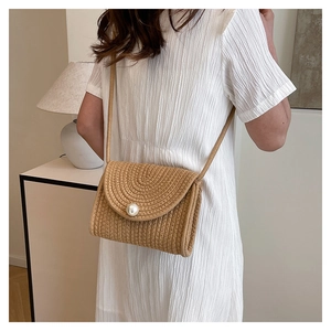 Close-up of woven straw crossbody bag with large pearl detail on a white summer dress