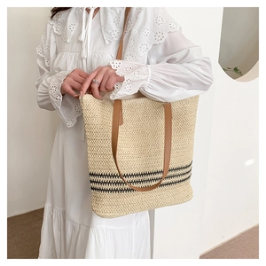 Close-up of woven straw tote bag featuring cream body and brown faux leather straps