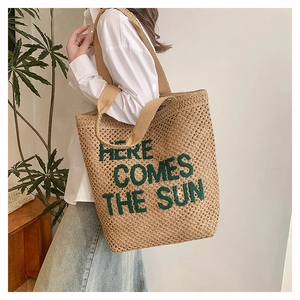 Detail of woven beach tote featuring green 'HERE COMES THE SUN' embroidery