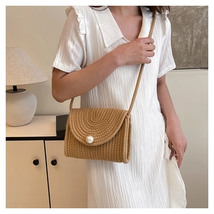 Detail of hand-woven straw crossbody bag featuring a large pearl clasp and rope strap