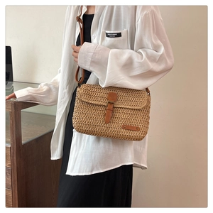Close-up of handmade straw woven crossbody bag with brown leather strap and buckle