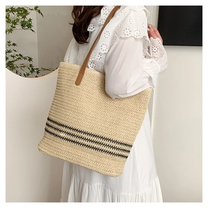 Close-up of woven straw tote bag featuring black stripes and brown leather strap