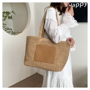 Detail of hand-woven straw tote bag with brown leather patch on white lace dress
