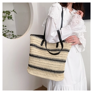 Detail of striped straw tote bag with black leather handles and woven paper texture