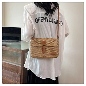 Detail view of woven straw crossbody bag with brown leather flap and adjustable strap