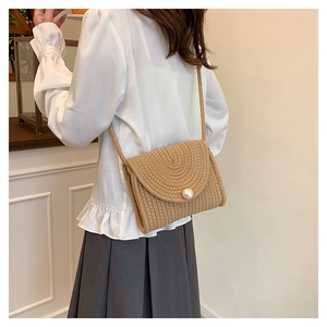 Detail of hand-woven straw crossbody bag with circular pearl accent and textured finish