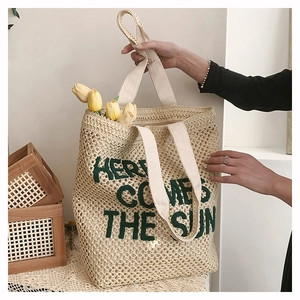 Close-up of woven straw tote bag featuring green Here Comes The Sun embroidered text