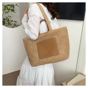 Detail of a large straw tote bag with brown leather patch and handles for summer