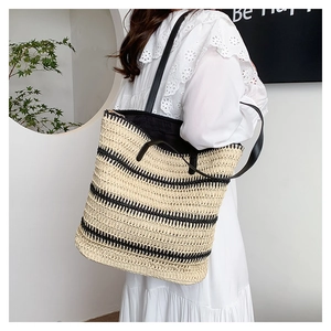 Detail of hand-woven straw tote bag with black and beige stripes worn with white dress