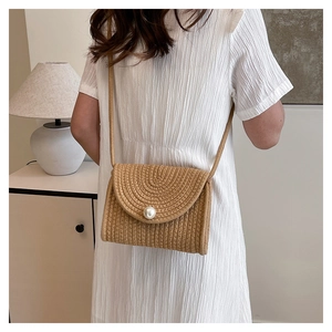 Detail of hand-woven straw crossbody bag with large pearl buckle decoration on a model