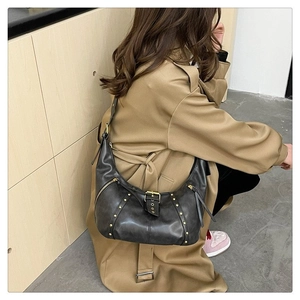 Détails du sac croissant vintage noir avec clous dorés et cuir texturé sur un trench-coat