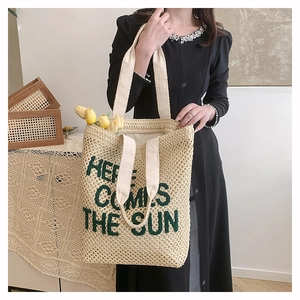 Detail of woven straw tote bag with Here Comes The Sun embroidery and wide fabric straps