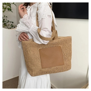 Close-up of summer straw tote bag with brown leather patch and woven texture detail