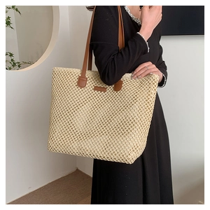 Detail of hand-woven straw tote bag with brown leather handles and stitched logo tag