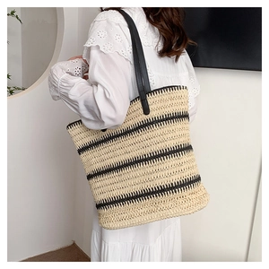 Detail of hand-woven straw tote bag with black stripes and leather shoulder straps