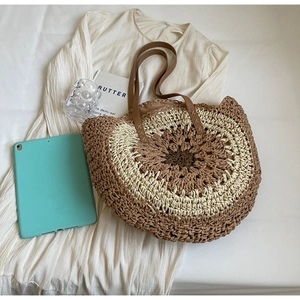 Detail of a round woven straw beach bag with a bicolor pattern and brown leather strap