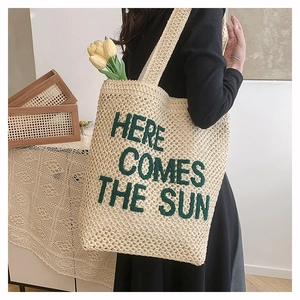 Detail of crochet woven tote bag with 'HERE COMES THE SUN' embroidery and long straps