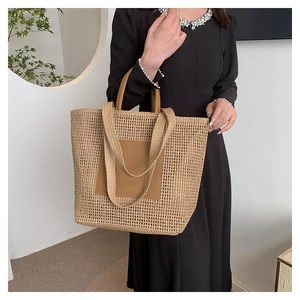 Close-up of summer straw tote bag with brown leather patch and dual handles worn by model