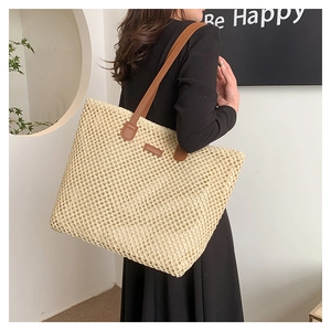 Close-up of woven beige straw tote bag with brown leather shoulder straps and decorative patch