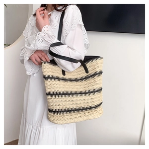 Detail of a large woven tote bag with black stripes and leather straps on model