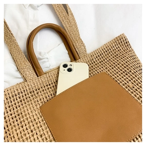 Macro detail of straw tote bag with brown leather pocket and white phone for size