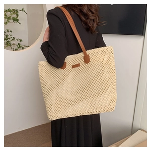 Detail of hand-woven straw tote with brown leather strap worn by a model in soft light